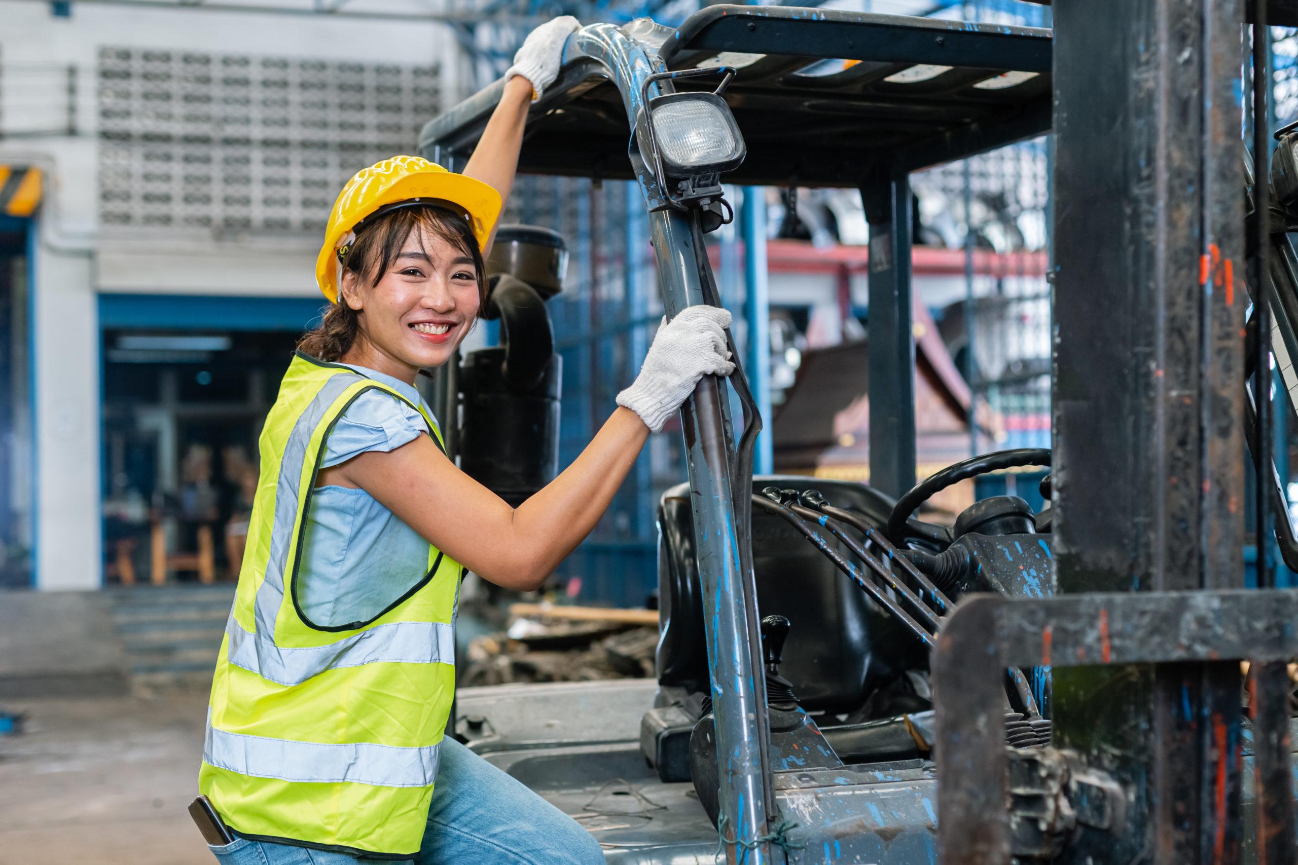 Female forklift operator pausing her work to pose for a photo next to the forklift.